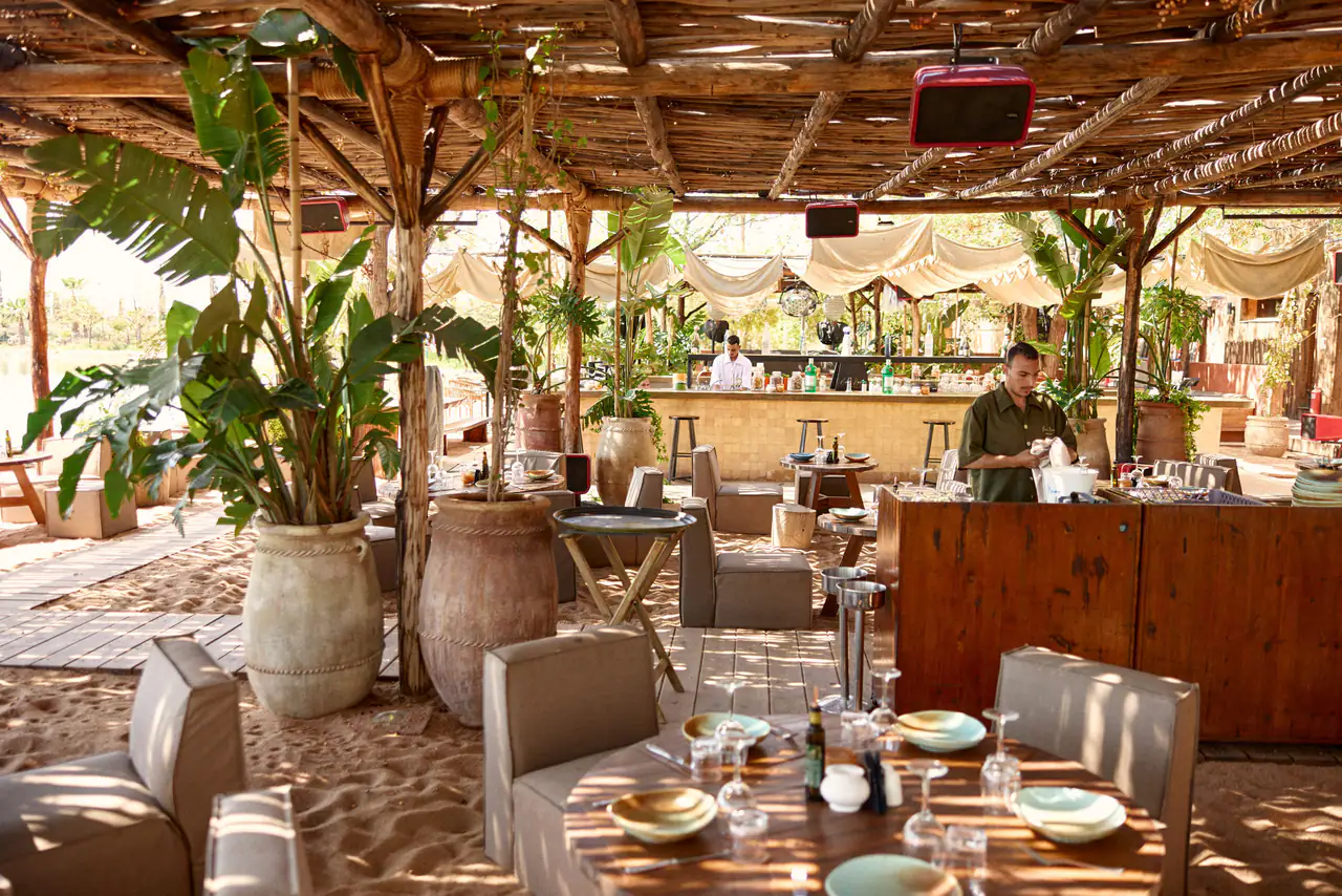 Tables dressées sous la pergola du restaurant, avec le bar en fond